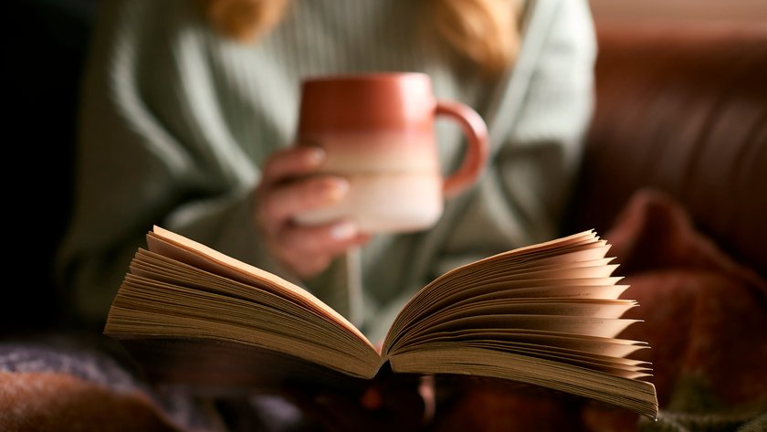 Eine Frau hält in der einen Hand ein aufgeschlagenes Buch und in der anderen eine Tasse