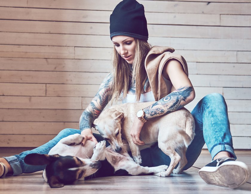 Frau mit Tattoos krault ihren Hund