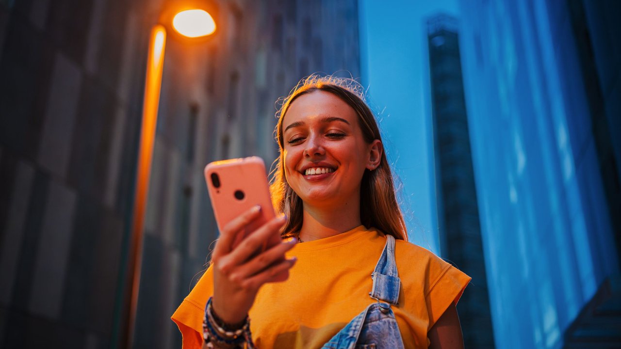 Eine junge Frau hält ein Smartphone und ist in der Dämmerung unterwegs