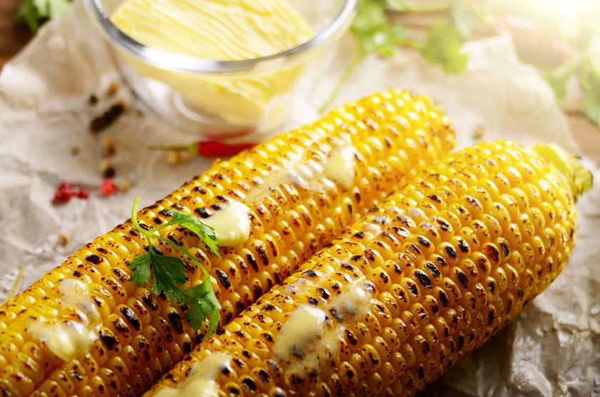 Grilled sweet corn cob with melting butter and greens on baking paper