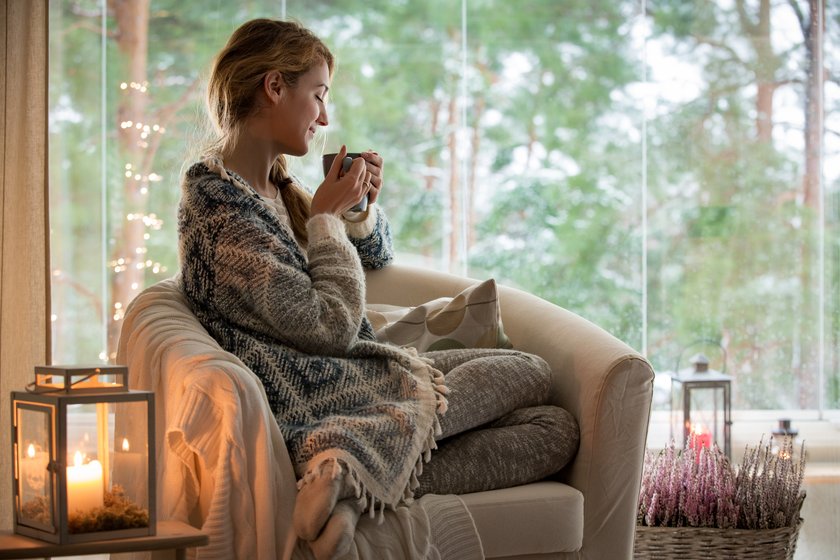 Frau sitzt frierend am Fenster und trinkt Tee