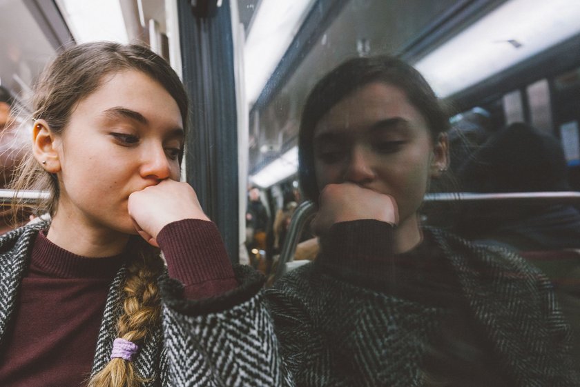 Junge Frau sitzt nachdenklich in einer U-Bahn und blickt in die Ferne.