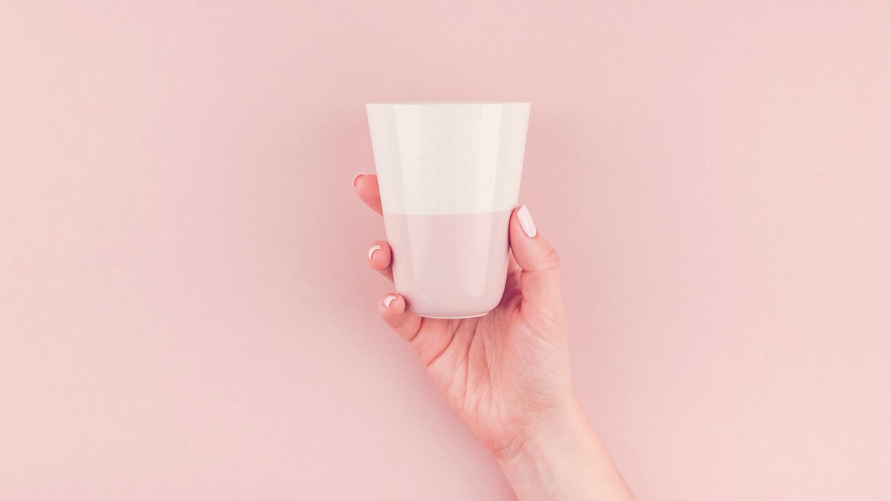 Creative image of woman hand holding coffee cup with copy space on millennial pink background in minimalism style. Concept template for feminine blog, social media