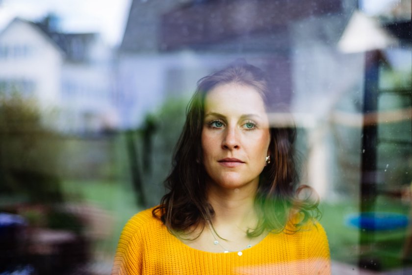 Young woman looks thoughtfully and sadly through the window into the garden with children's toys.