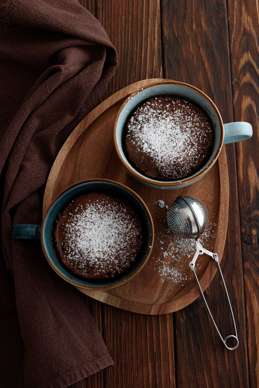 Two chocolate mug cake  under sugar icing on dark wooden table. Easy homemade dessert. Mugcake from microwave. Top view