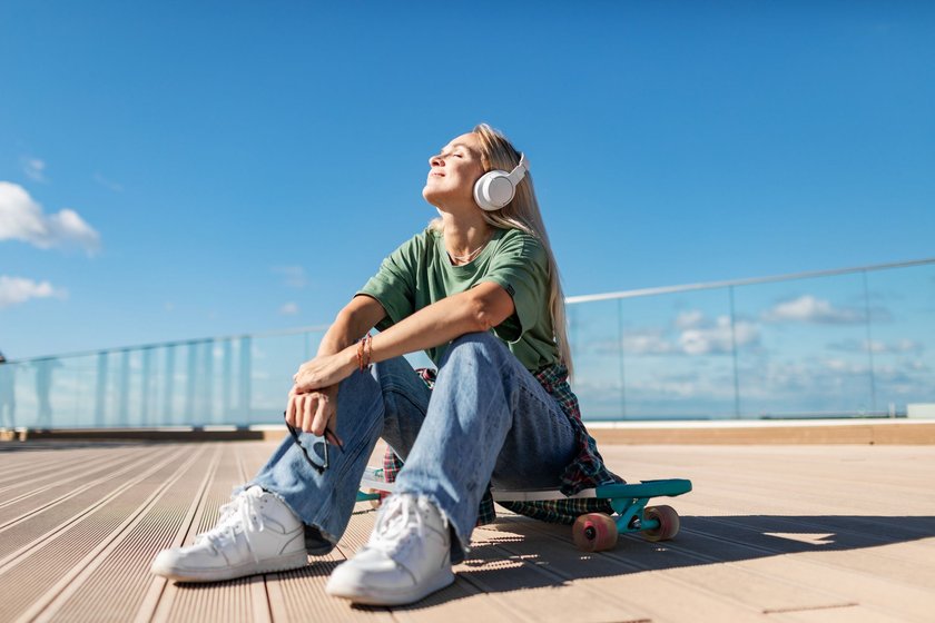 Mid adult woman sitting on longboard and listening to music using headphones
