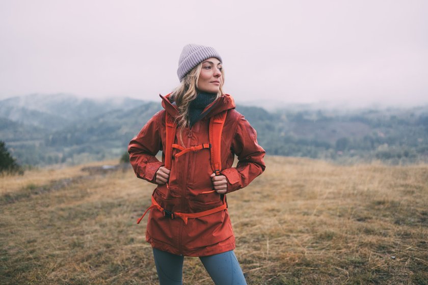 Eine Frau mit roter Jacke und rotem Rucksack ist auf einer Wanderung in der Natur