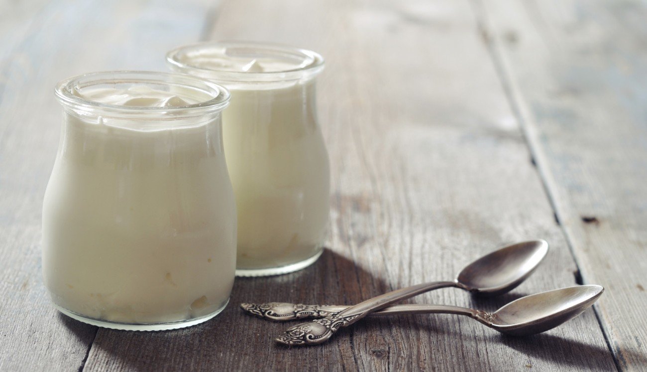 Greek yogurt in a glass jars with spoons on wooden background