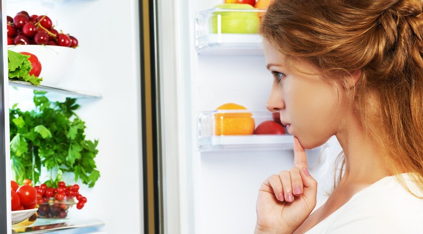 Frau überlegt vorm Kühlschrank