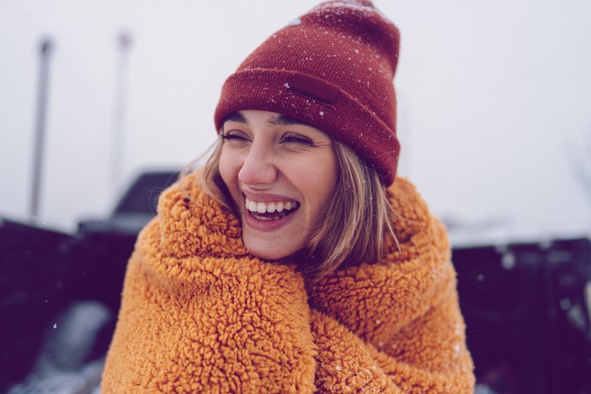 Lachende Frau mit Mütze und Decke im Schnee