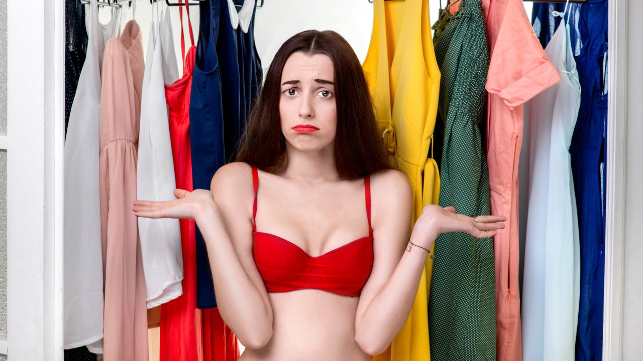 Young woman in underwear thinking what dress to wear in front of the clothes in wardrobe. Nothing to wear concept