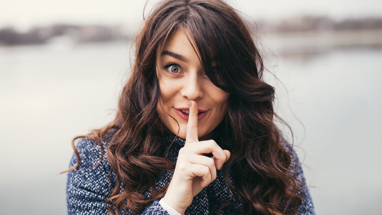 cute woman with long black hair holding her finger on her mouth as she was keeping a secret