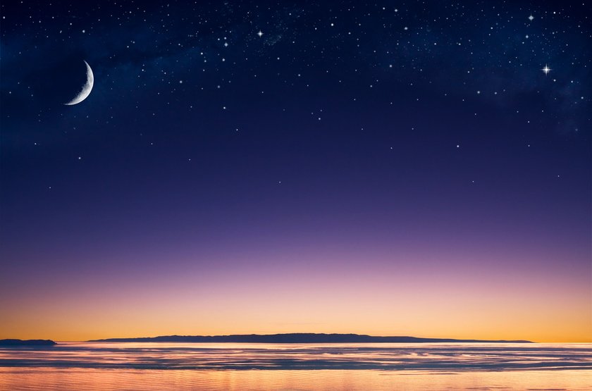 A crescent moon and stars over an island in the Pacific ocean just after sunset.