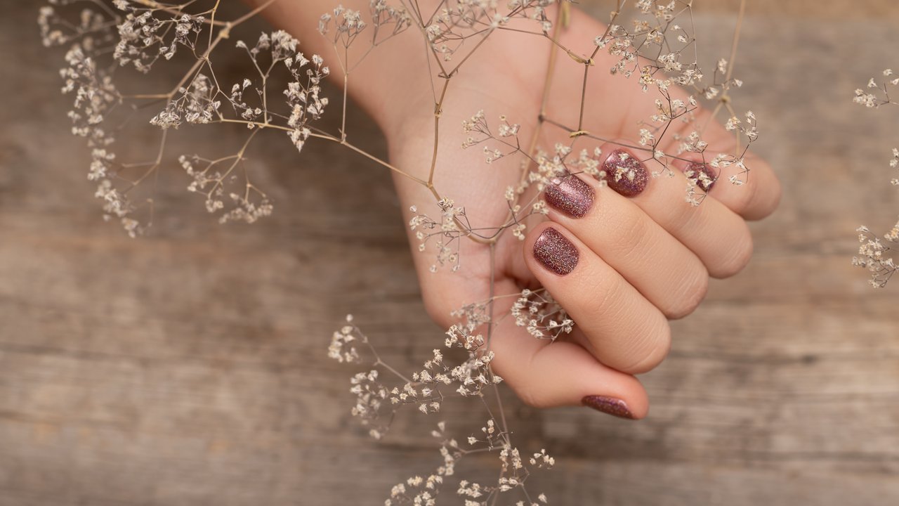 Female hand with glitter brown nail design. Girl hand hold autumn flower Brown nail polish manicure with star nail art