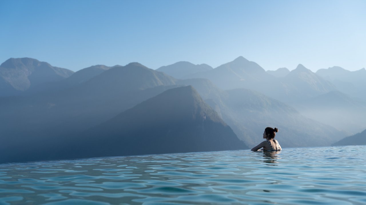 Sexy woman relaxing in infinity swimming pool   looking at stunning mountain view at  luxurious resort / vacation concept