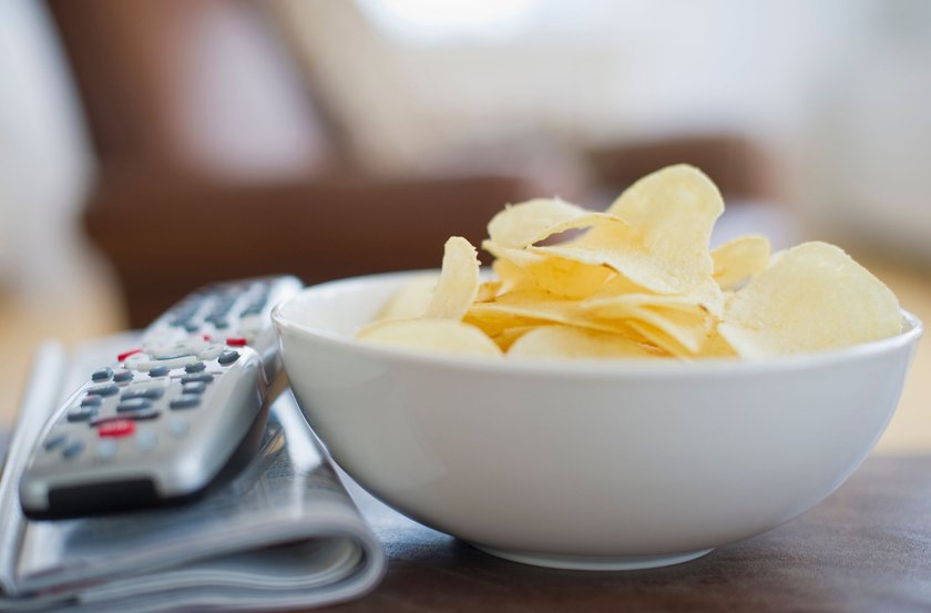 Eine Schüssel mit Chips steht auf einem Sofatisch und daneben liegt eine Fernbedienung.