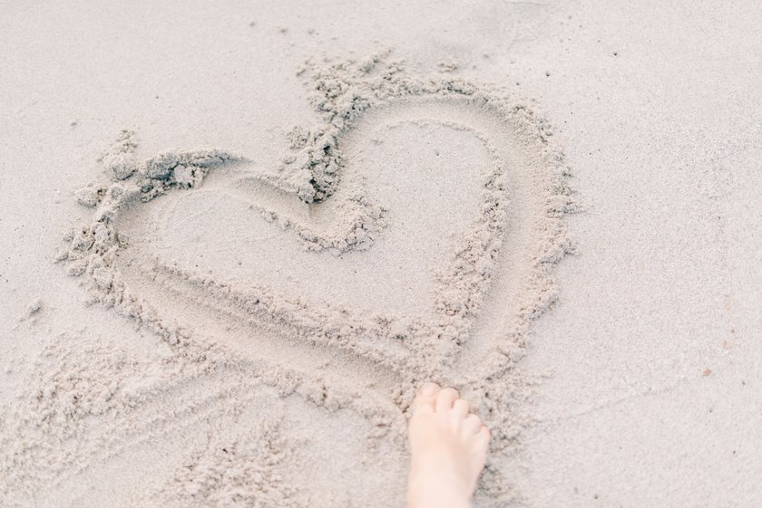 Jemand malt mit seinem Fuß ein Herz in den Sand