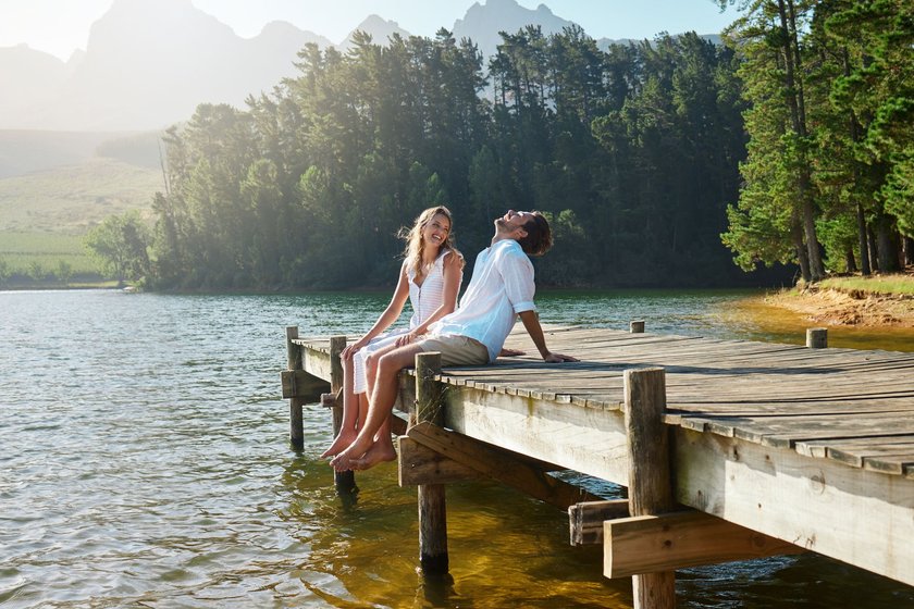Ein verliebtes Paar sitzt auf einem Steg an einem See und lacht