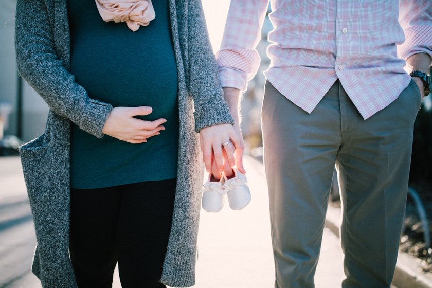 Schwangere Frau hält die Hand ihres Mannes und kleine Babyschuhe
