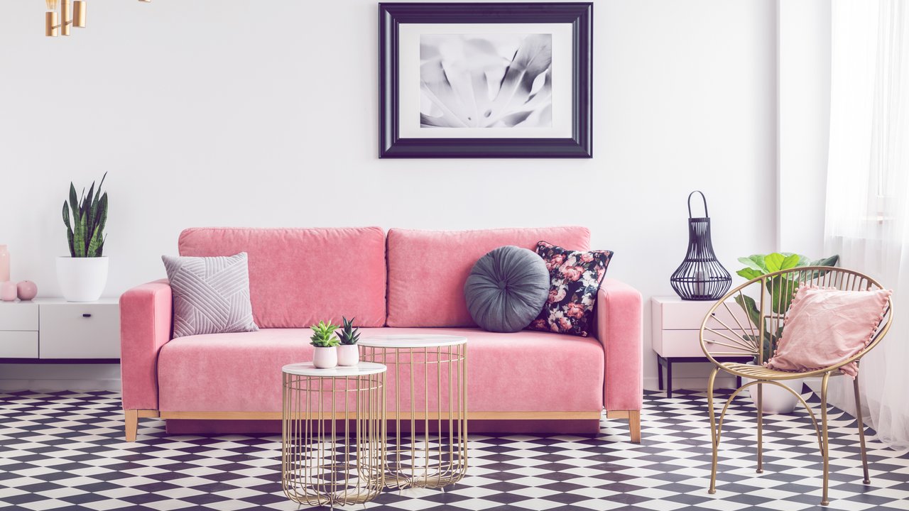 Glamour living room interior with a pink sofa, golden armchair and tables, painting and checkered tiles. Real photo