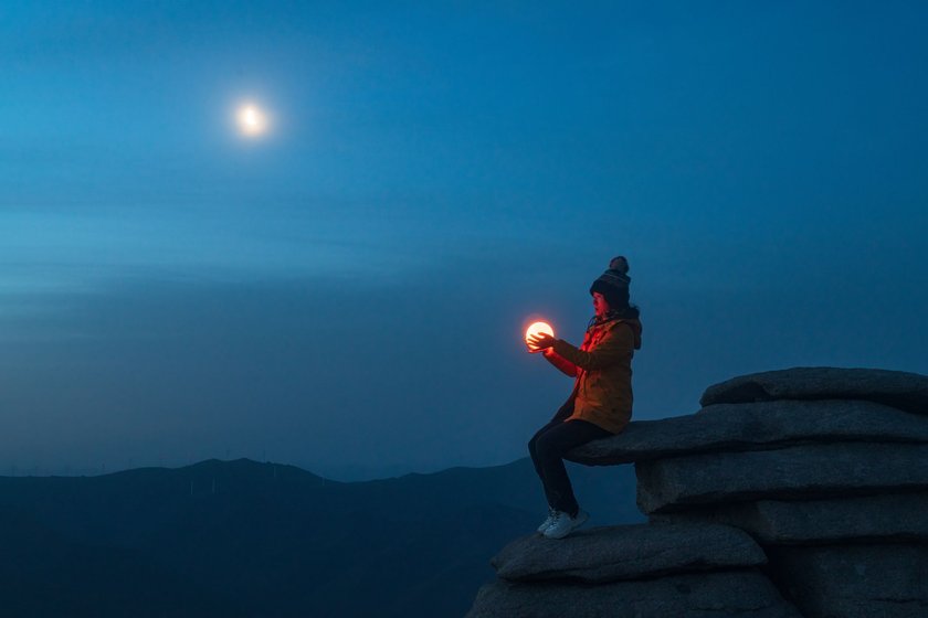 Eine junge Frau sitzt auf einem Stein und hält eine Lampe