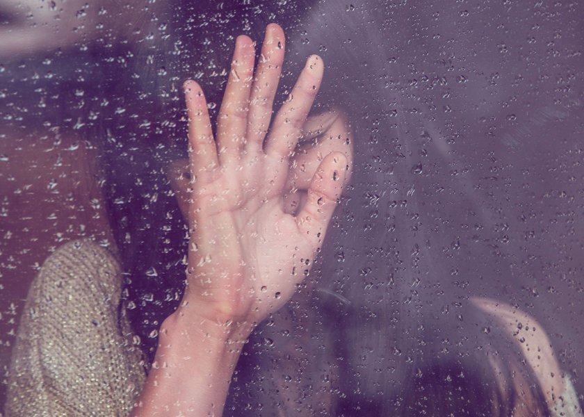 Eine Frau lehnt an einem Fenster, auf dem Regentropfen zu sehen sind