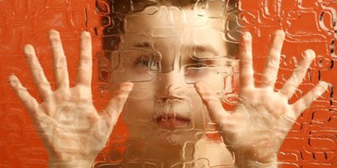 Junge mit Autismus steht hinter Glasscheibe Junge mit Autismus steht hinter Glasscheibe