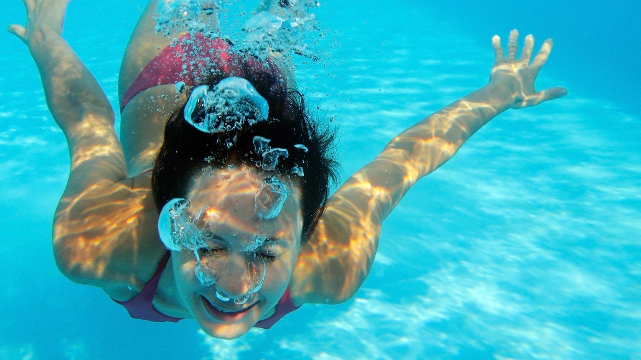 Woman swimming underwater in pool smiling. Young female swimmer  at holiday resort.