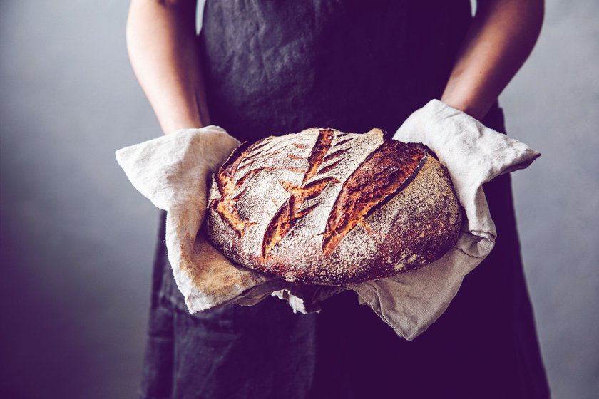 Midsection of woman holding fresh baked sourdough bread. Close-up of homemade wheat and rye beard. She is in kitchen.