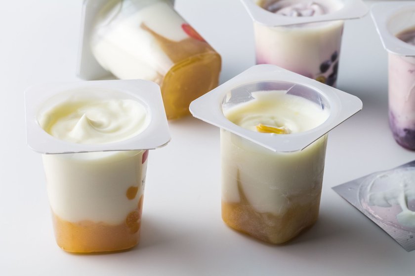 Fruit flavoured yogurt in transparent plastic cups on white background with silver foil lid - Yoghurt cup background with selective focus