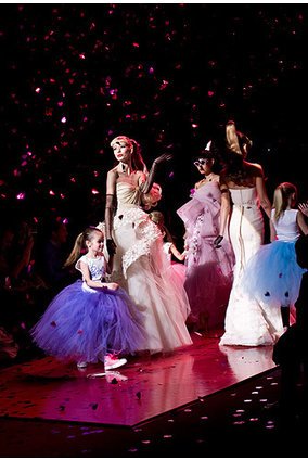 Einige Models mit kleinen Kindern in Tüllkleidern auf dem Laufsteg. Von der Decke rieseln pinke Herzen Einige Models mit kleinen Kindern in Tüllkleidern auf dem Laufsteg. Von der Decke rieseln pinke Herzen