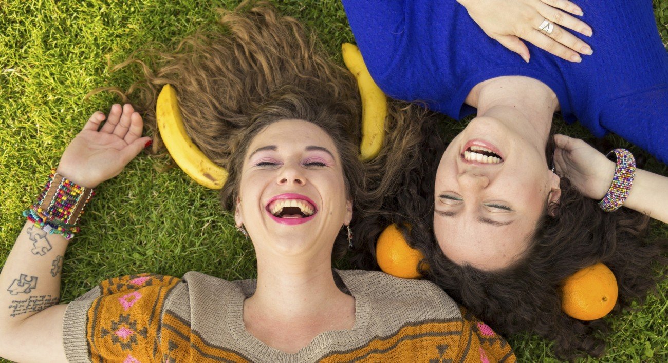 Above view of smiling happy girls, laying on a grass. Making fun with bananas, and oranges. Above view of smiling happy girls, laying on a grass. Making fun with bananas, and oranges.