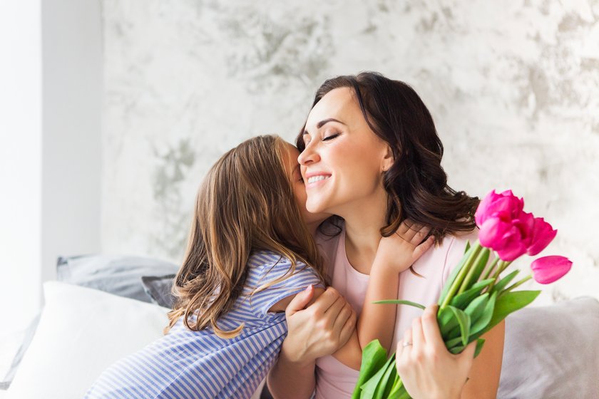 Tockter küsst Mutter auf die Wange, Mutter hält Blumen in der Hand und freut sich