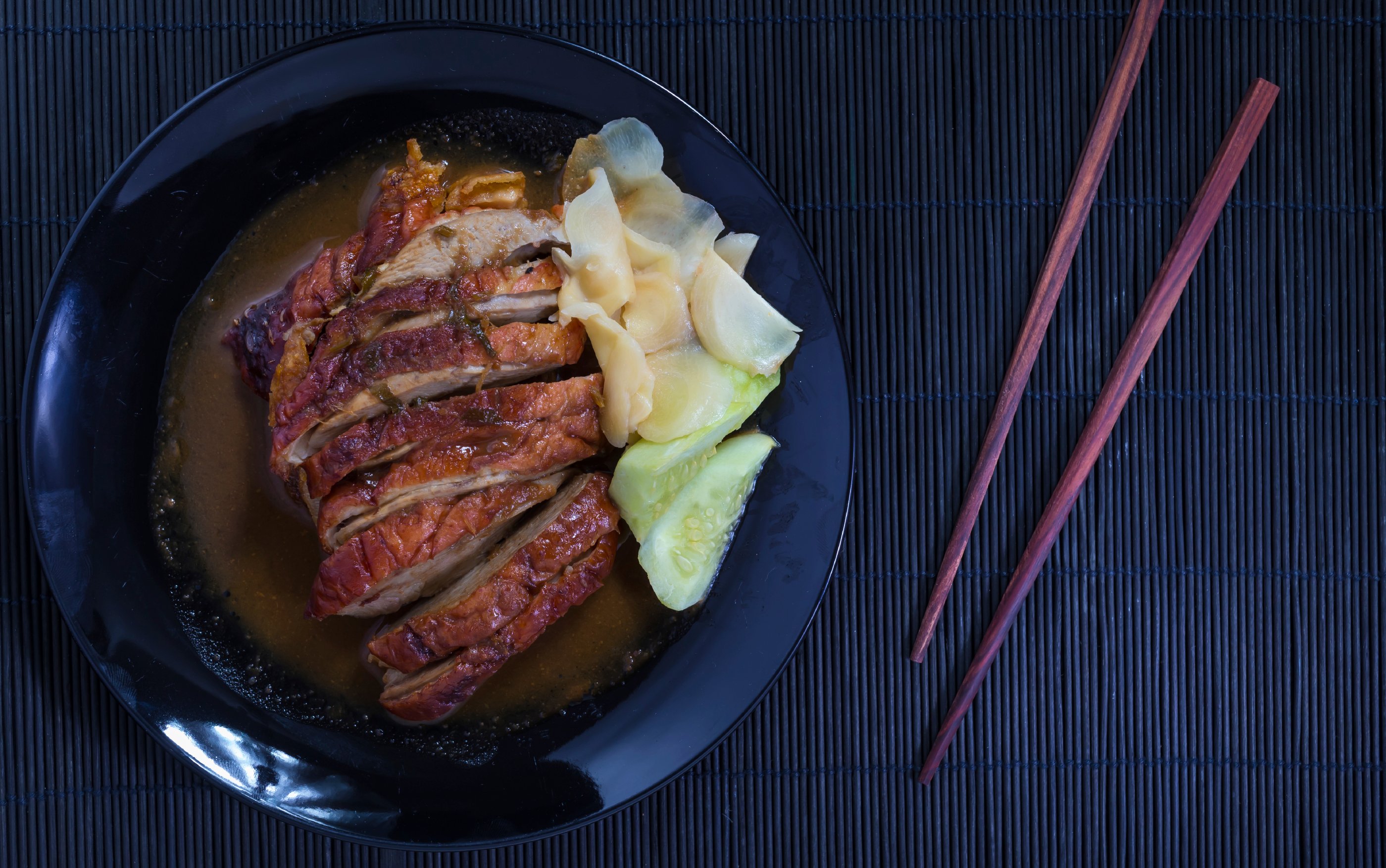 Roast duck and sauces in black dish with chopsticks over Black Sushi mat