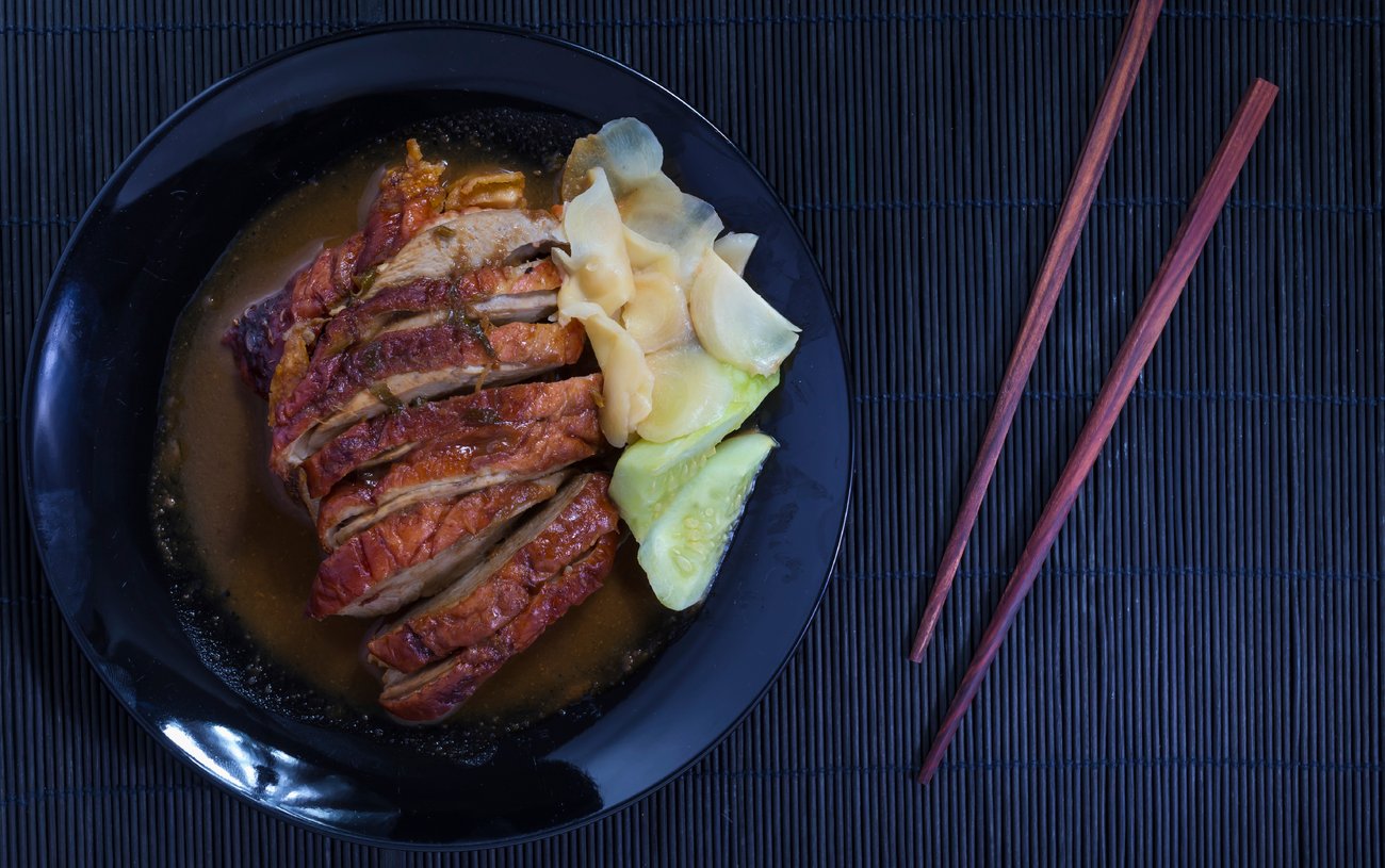 Roast duck and sauces in black dish with chopsticks over Black Sushi mat Roast duck and sauces in black dish with chopsticks over Black Sushi mat
