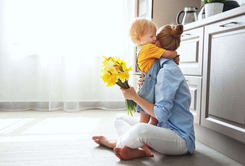 Kleiner Junge umarmt seine Mutter in der Küche nachdem er ihr Blumen geschenkt hat