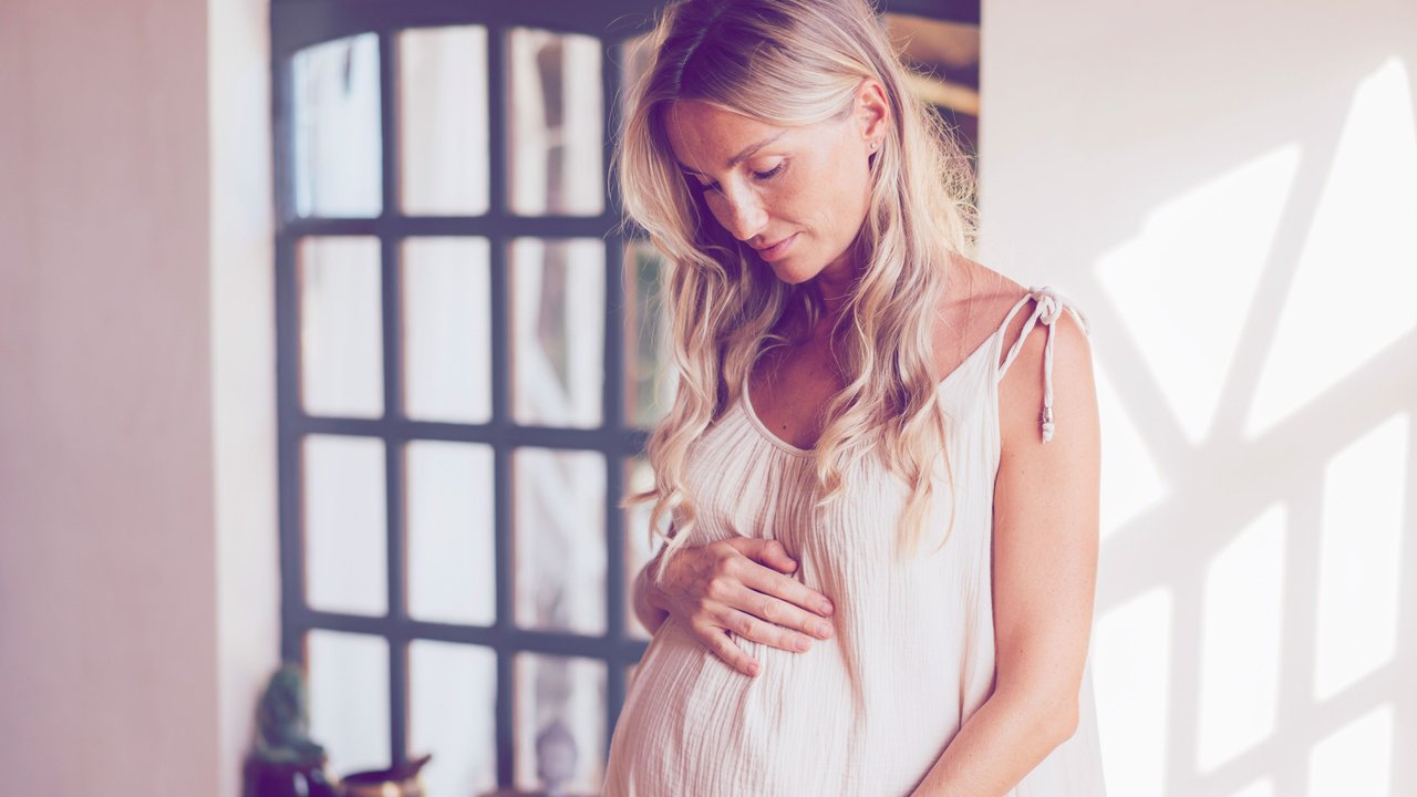 Beautiful pregnant woman touching her belly standing by the window