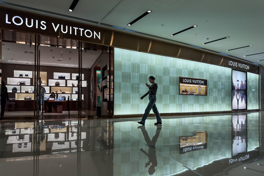 CHONGQING, CHINA - JUNE 04: A woman walks past a Louis Vuitton boutique in a luxury shopping mall, with the illuminated storefront, digital displays, and designer products visible inside the store, on June 04, 2025 in Chongqing, China.  (Photo by Cheng Xin/Getty Images)
