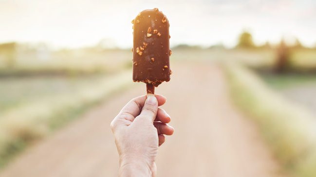 Hand of woman holding a chocolate popsicle on nature background