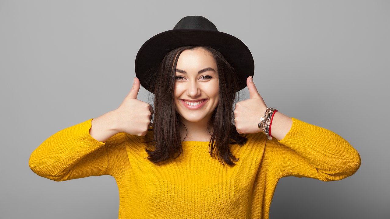 Portrait of trendy young  woman showing thumb up over grey background