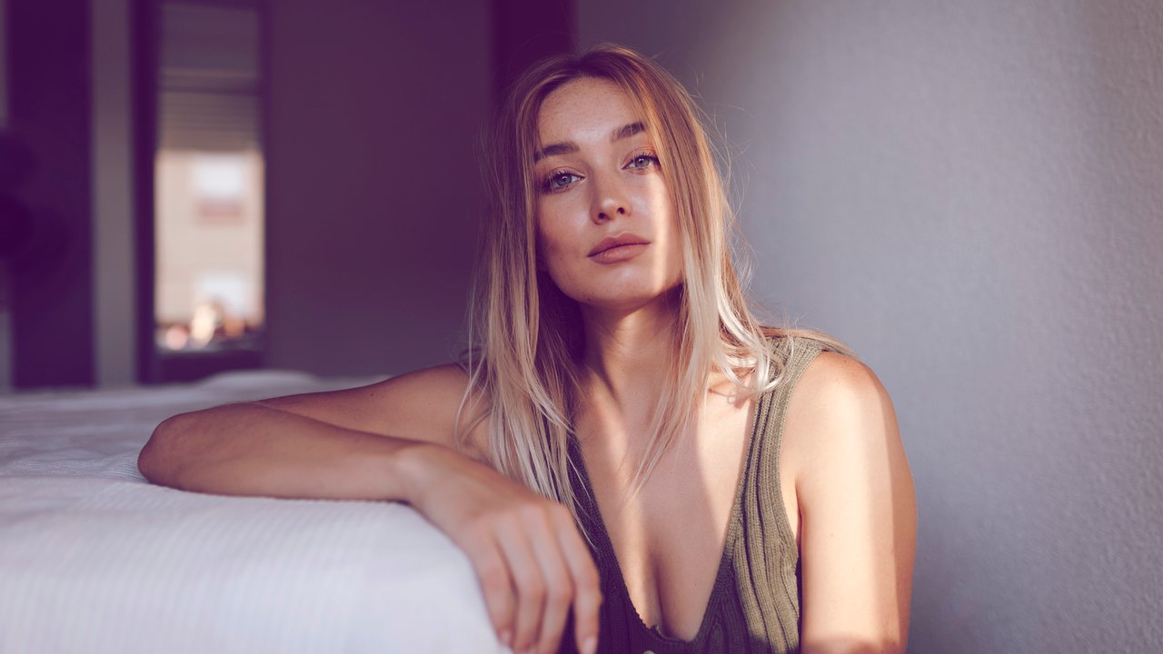 Portrait of blonde woman leaning on bed with sunlight on her face in Granada, Spain