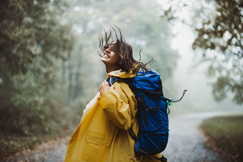 Eine Frau in einer gelben Regenjacke ist glücklich an einem Herbsttag unterwegs