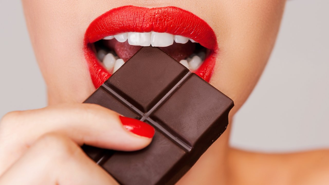Indulging in a sweet affair with chocolate. Close-up of a beautiful women holding finger on her red lips while standing against grey background