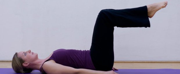 Schritt 1 der Pilatesübung Single Leg Stretch, bei der die Pilateslehrerin auf dem Rücken liegt
