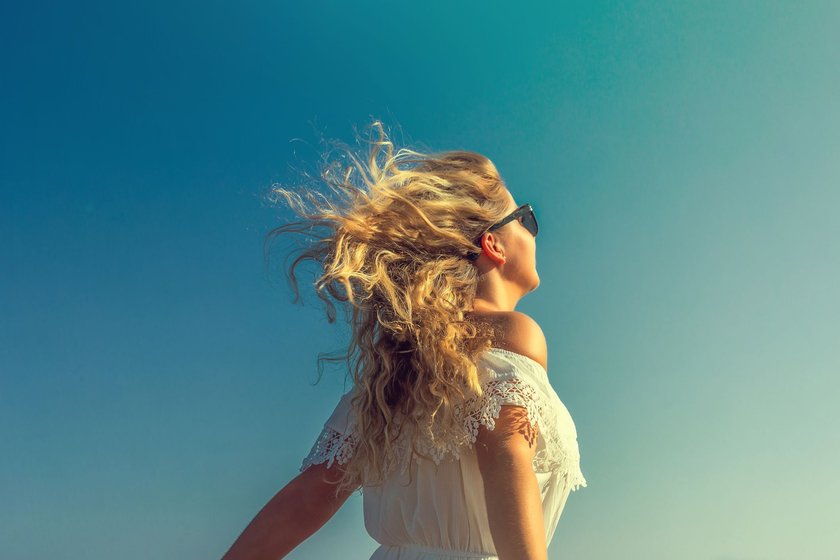 Eine Frau mit wehendem Haar genießt die Sonnenstrahlen am Strand.