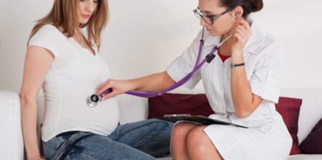 Hebamme untersucht Babybauch mit Stetoskop Hebamme untersucht Babybauch mit Stetoskop
