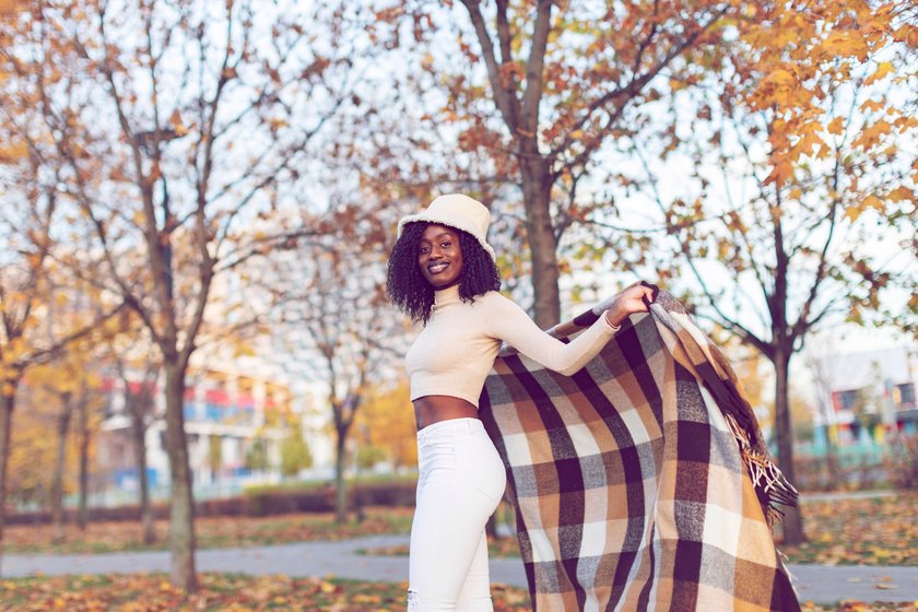 Young adult Black female in warm poncho relaxing in autumn park