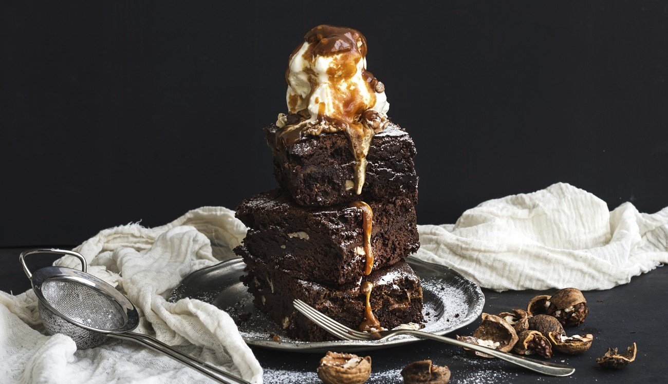 Fudgy Brownies tower with salted caramel, walnuts and ice-cream on vintage metal plate. Dark backdrop