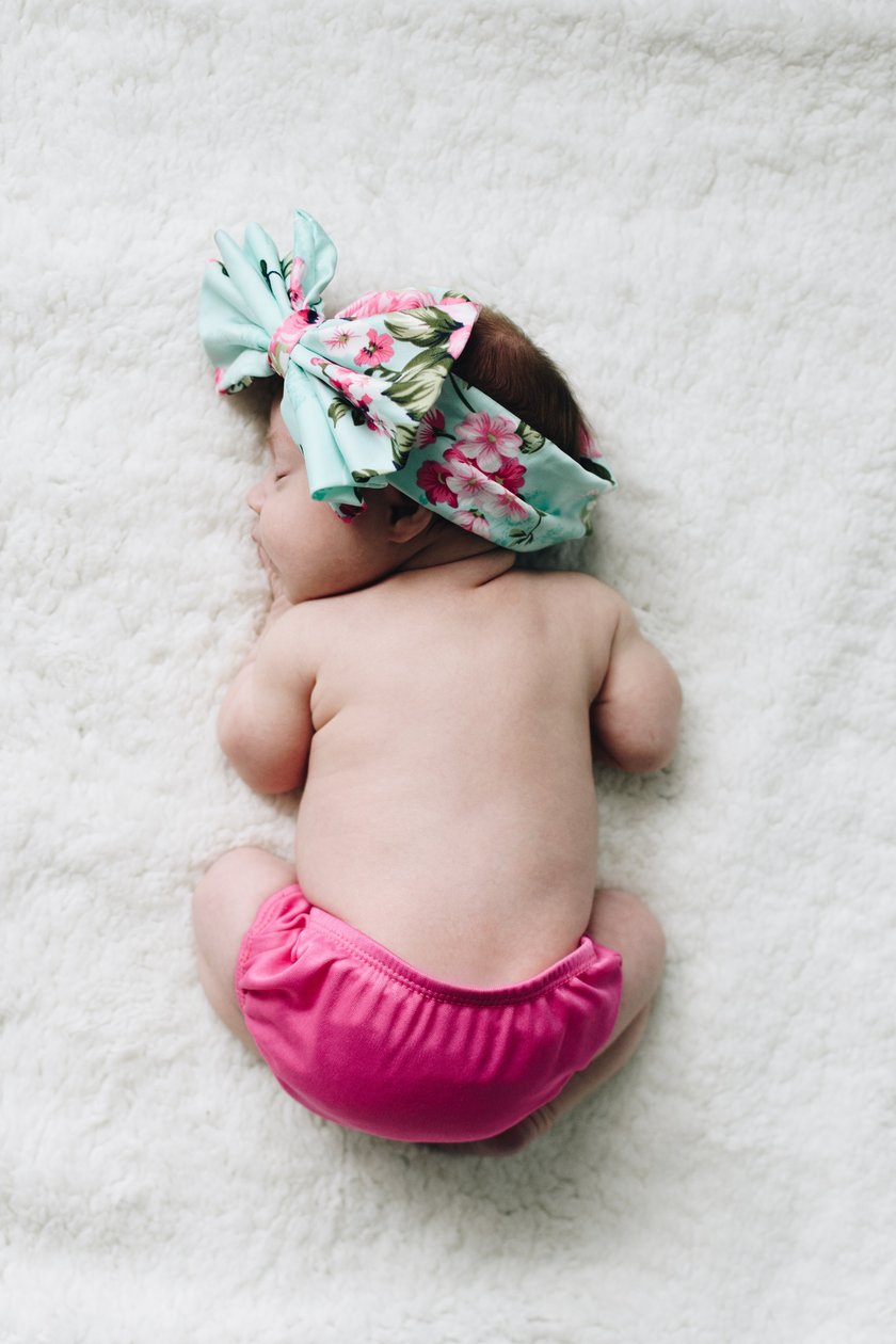 Baby mit Schleife im Haar liegt auf dem Bauch und schläft