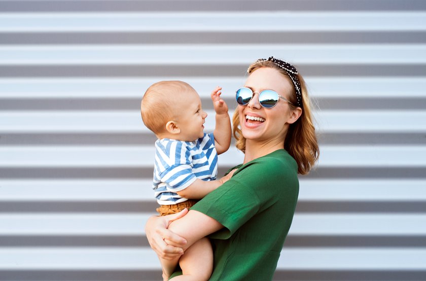 Frau hat Kind auf dem Arm, dass versucht die Sonnenbrille wegzunehmen, beide lachen